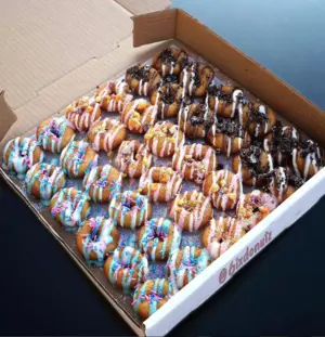 A box of assorted mini donuts decorated with colorful icing and sprinkles.