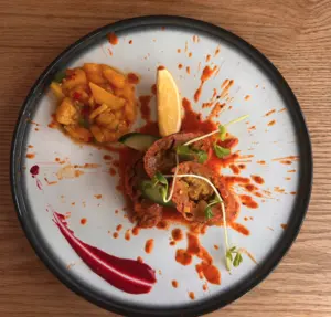 Artfully plated gourmet dish with sauce splatters, diced fruit salad, and a lemon wedge on a white plate.