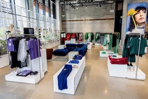 Modern clothing store interior with neatly arranged clothes, bright lighting, and a large portrait on the wall.