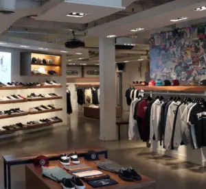 Clothing and sneaker store interior with shelves of shoes, hanging shirts, and folded apparel on tables.