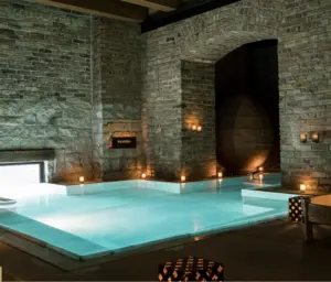 Indoor stone-walled spa pool with soft lighting and candles creating a relaxing atmosphere.