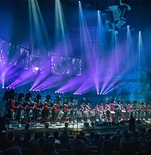 A pipe band performs on stage with dramatic purple lighting and an audience watching.