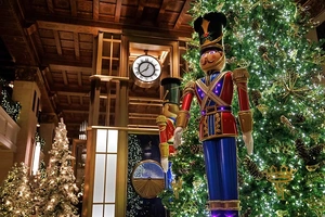Festive lobby with large nutcracker, decorated Christmas trees, and a clock on the wooden wall in the background.