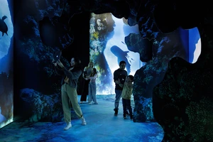 People explore an immersive, underwater-themed exhibit with blue lighting and projected sea creatures.