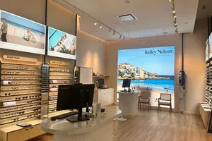 Interior of an eyeglass store with display shelves, two desks, and beach-themed wall posters.