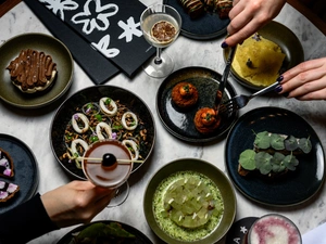 Table set with various gourmet dishes, cocktails, and two people’s hands reaching for food.