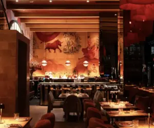 Dimly lit restaurant with mural art on the wall, cozy seating, and tables set for dining.