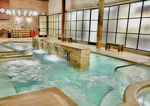 Indoor spa pool with stone waterfall feature, warm lighting, and frosted glass walls for a relaxing atmosphere.