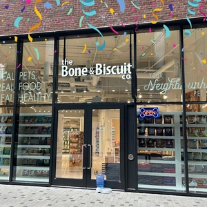 Storefront of The Bone & Biscuit Co. with glass windows and an open sign, decorated with colorful confetti.