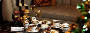 Elegant afternoon tea setup with pastries, desserts, and teacups on a table beside a sofa and festive decor.