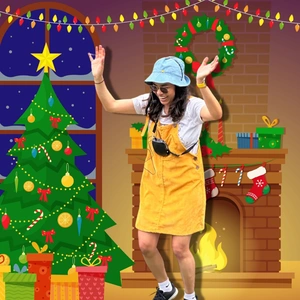 Woman in yellow dress and blue hat dancing in front of a Christmas tree and fireplace with decorations.