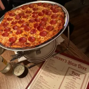 A pepperoni pizza on a metal stand next to a menu at a restaurant called Cherry’s High Dive.