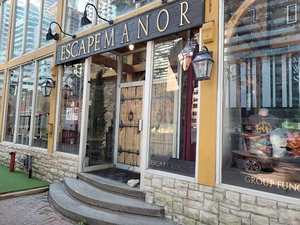 Entrance of Escape Manor with large wooden doors and glass windows, set in a stone and yellow building exterior.
