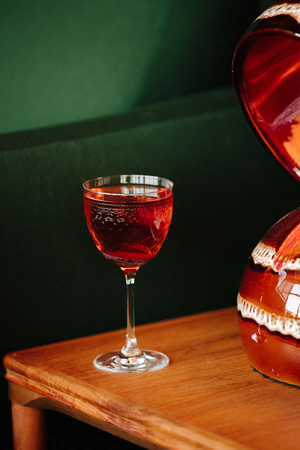 A glass of red wine on a wooden table with a green background and a decorative object beside it.