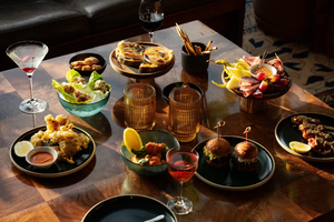 A wooden table set with assorted appetizers, drinks, and small plates in warm, natural light.