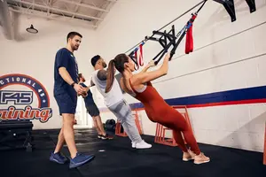 Three people exercise using suspension straps while an instructor supervises in a gym with “F45 Training” on the wall.