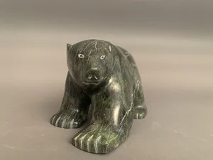 A polished dark stone sculpture of a bear with white eyes, positioned on a neutral background.