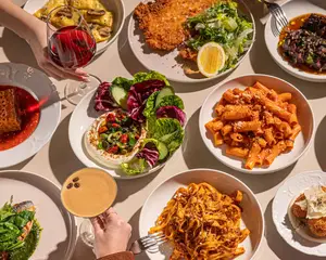 A table with assorted Italian dishes, salads, pasta, and drinks, including red wine and a cocktail.