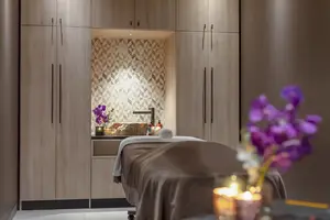 A spa room with a massage table, soft lighting, flowers, and wooden cabinets in the background.
