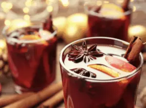 Glasses of mulled wine with orange slices, star anise, and cinnamon sticks, with festive lights in the background.