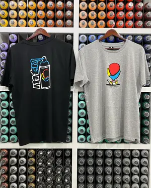 Two graphic t-shirts hang on a wall in front of shelves filled with colorful spray paint cans.