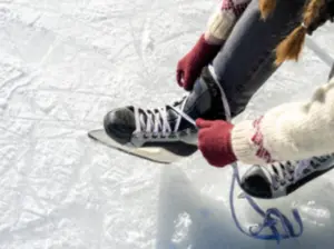 Person in red gloves ties the laces of their ice skates while sitting on an outdoor ice rink.