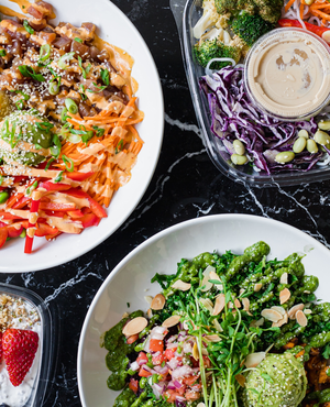 Colorful salads and bowls with vegetables, grains, and dressings on a black marble table.