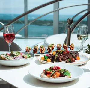 Three plates of gourmet food and two glasses of wine on a table with a scenic view in the background.