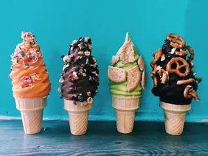 Four colorful ice cream cones with various toppings against a blue background, lined up on a wooden surface.