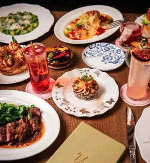 A table set with assorted gourmet dishes, desserts, and colorful drinks on elegant plates and glasses.