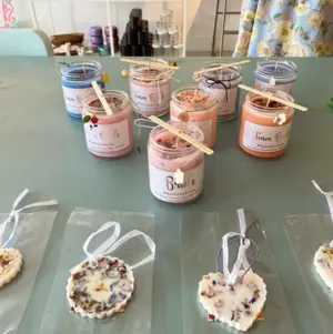 Colorful candles in jars and floral wax ornaments displayed on a light blue table.