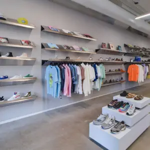 Clothing and sneakers displayed on shelves and racks in a modern retail store with a minimalist design.