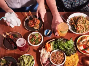 Two people sharing a table filled with various colorful dishes and drinks, seen from above.