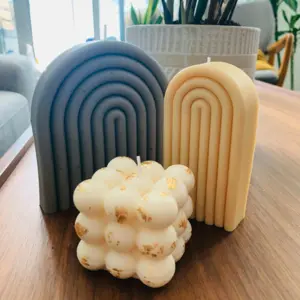 Three decorative candles: two arch-shaped (gray and cream) and one white bubble candle with gold flecks.