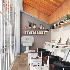 Modern nail salon with white chairs, black foot basins, potted plants, and a slanted wooden ceiling.