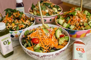 Four colorful salad bowls with fresh veggies, avocado, and dressing bottles on a marble table.