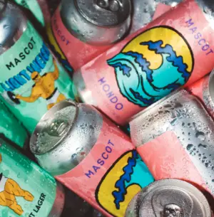 Colorful Mascot beer cans with graphic designs, stacked together and covered in condensation.