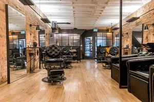 Modern barbershop with wooden floors, brick walls, mirrors, and empty black barber chairs.