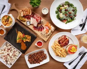 Assorted dishes including salad, fries, burger, charcuterie board, beans, rice, and stuffed pastry on a table.