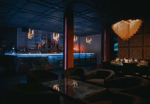 Dimly lit lounge with a glowing bar, modern chandeliers, and dark seating areas.