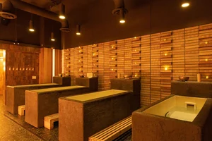 Modern spa room with stone massage tables, wooden benches, warm lighting, and wood-paneled walls.