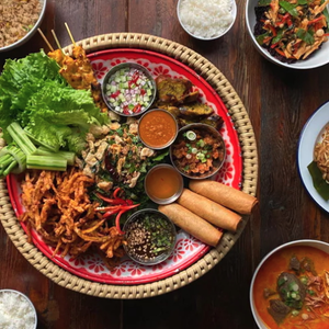 A vibrant Thai platter with spring rolls, salads, dips, grilled meat, and assorted vegetables on a wooden table.