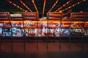 Four bar stools in front of a colorful, graffiti-covered bar counter with warm lighting above.