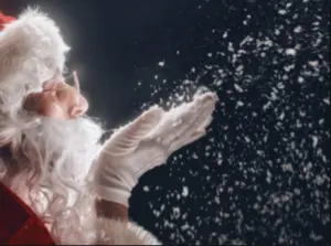 Santa Claus blowing snow from his gloved hand against a dark background.