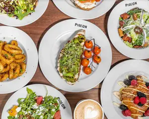 Seven plates with various dishes and a latte on a wooden table, viewed from above.