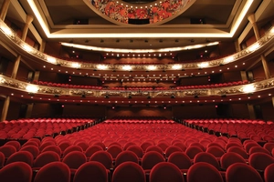 Empty theater with rows of red seats, balconies, and ornate ceiling decorations, viewed from the stage.