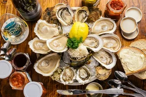 A plate of fresh oysters on ice with lemon, sauces, bread, and utensils on a wooden table.