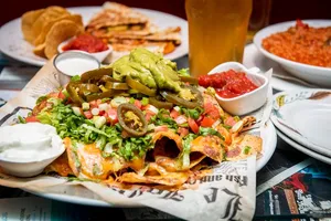 A plate of loaded nachos with guacamole, jalapeños, salsa, and sour cream, with quesadillas and rice nearby.