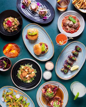 A variety of colorful dishes, sliders, salads, and drinks arranged on a dark blue tabletop.