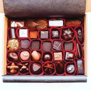 A box of assorted chocolates arranged in rows with various shapes and decorative toppings.